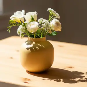 Elegant butter yellow vase with fresh white roses and freesias on a light wooden table, illuminated by natural sunlight, bringing serene joy to a home space.