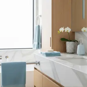 Contemporary bathroom vanity with marble countertop, wooden cabinetry, ice blue towels, and a delicate white orchid, showcasing revitalizing freshness in pastel home interiors.