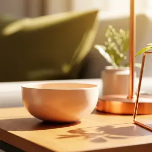 Close-up of a delicate light peach decorative bowl on a wooden surface, with soft, warm natural light and blurred green accents in the background, conveying enveloping warmth in home decor.