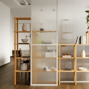 A bright studio apartment featuring an open shelving unit used as a stylish room divider, showcasing decorative items and plants while allowing light to pass through.